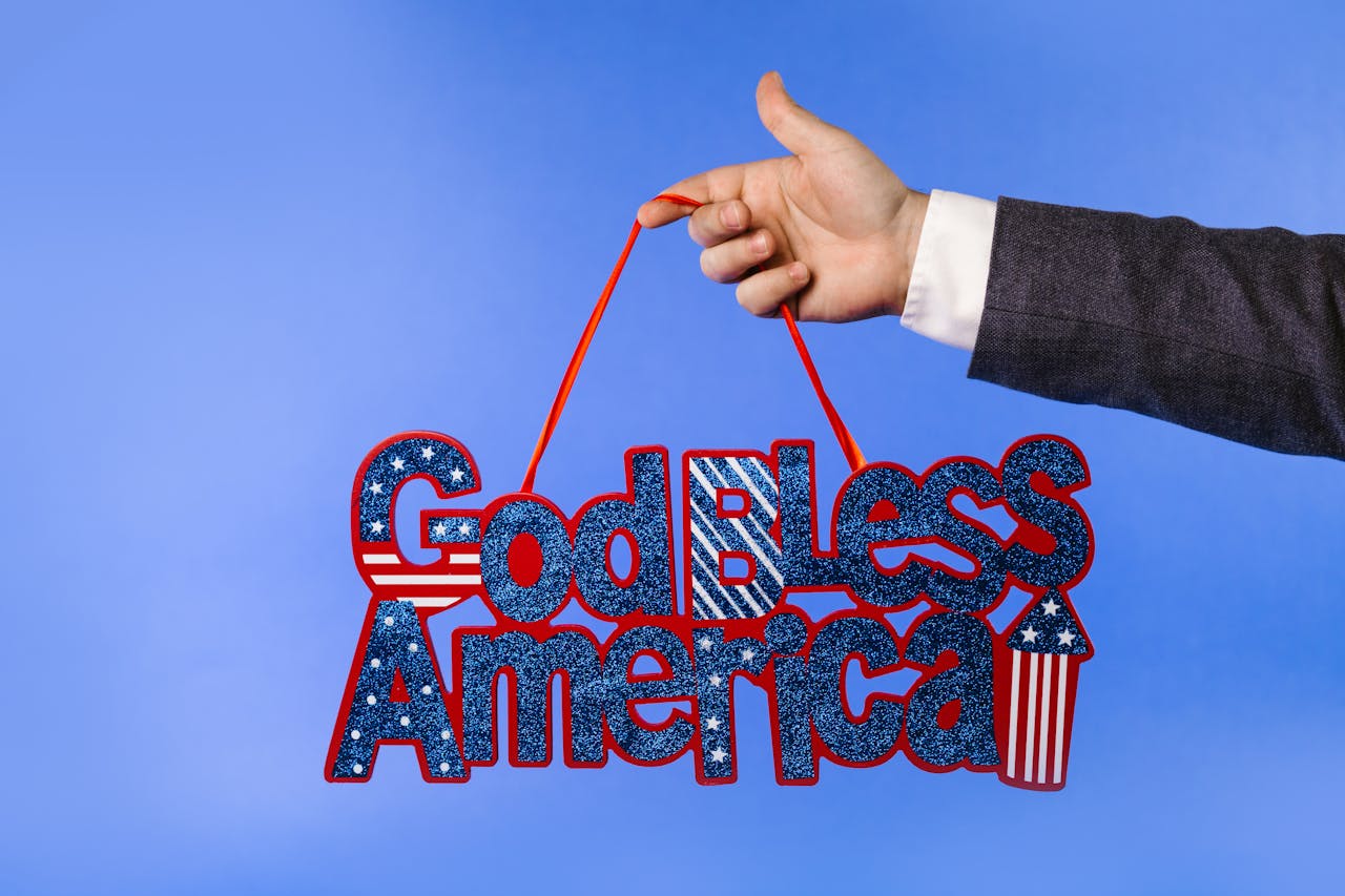 A businessman holds a glittery 'God Bless America' sign against a blue background, symbolizing patriotism.