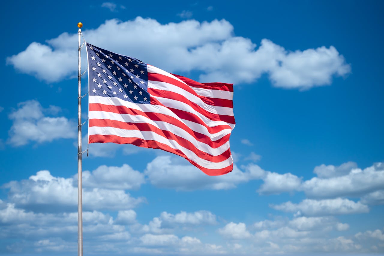 Vibrant American flag flying with a bright blue sky and fluffy clouds in the background.